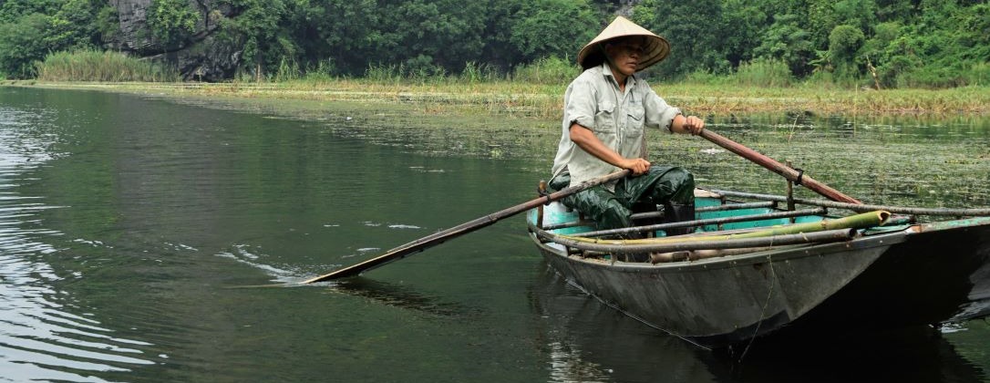 a vietnamese man paddling a row boat down a river.