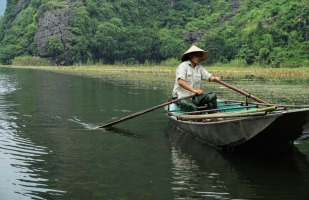 a vietnamese man paddling a row boat down a river.