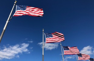 5 american flags flying in the sky on a beautiful day.