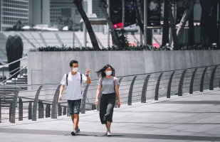 two pedestrians walking on a sidewalk wearing personal protective masks to prevent coronavirus spread.